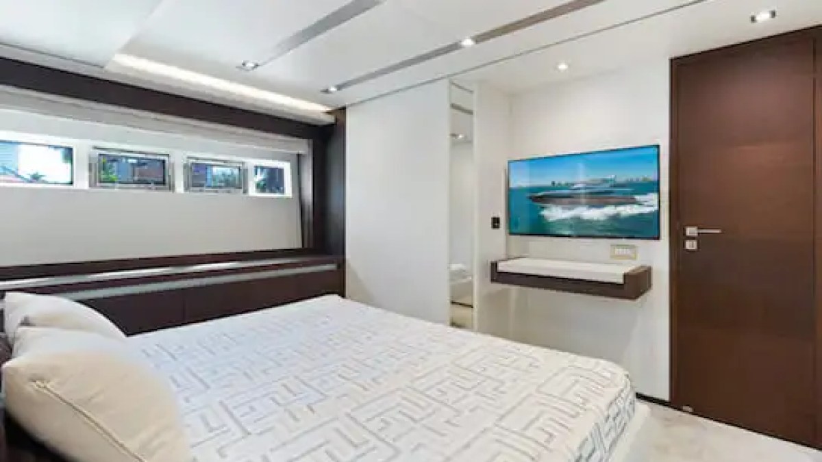 Modern bedroom on a yacht with a bed, small windows, TV, and sleek decor.
