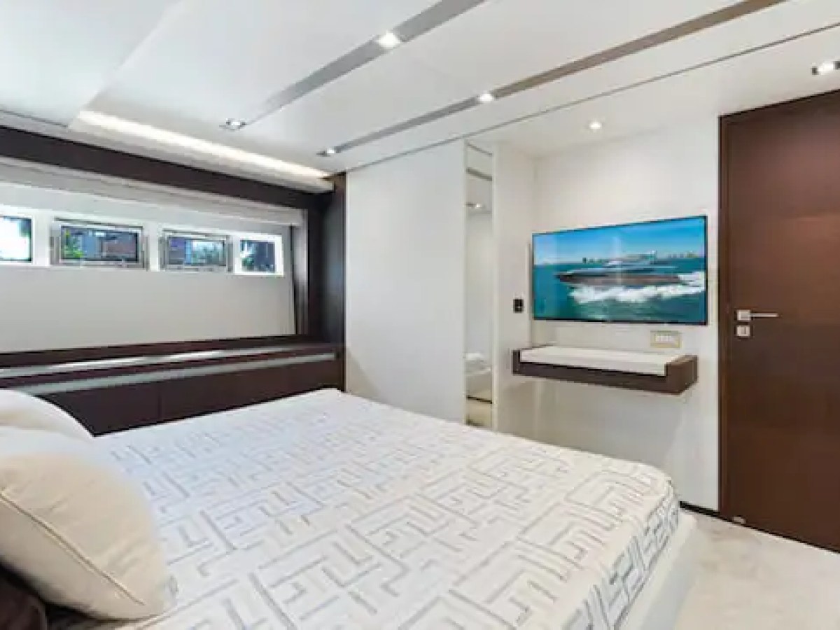 Modern bedroom on a yacht with a bed, small windows, TV, and sleek decor.