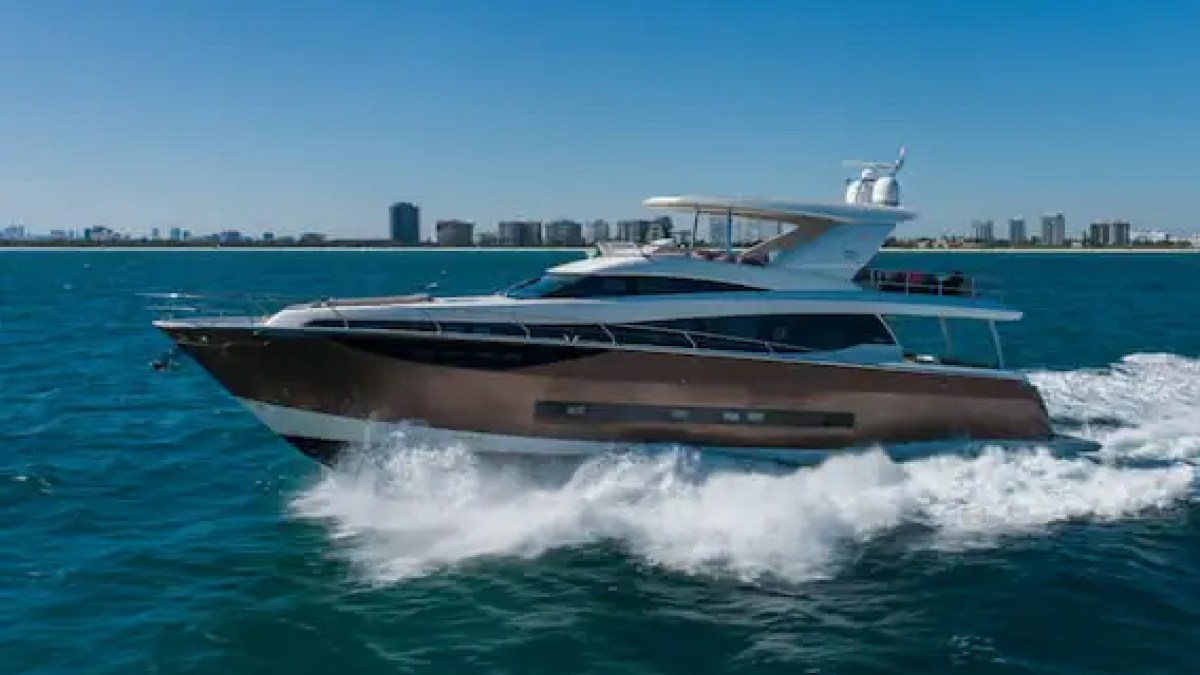 Luxurious cabin cruiser yacht gliding on open sea with city skyline in background.