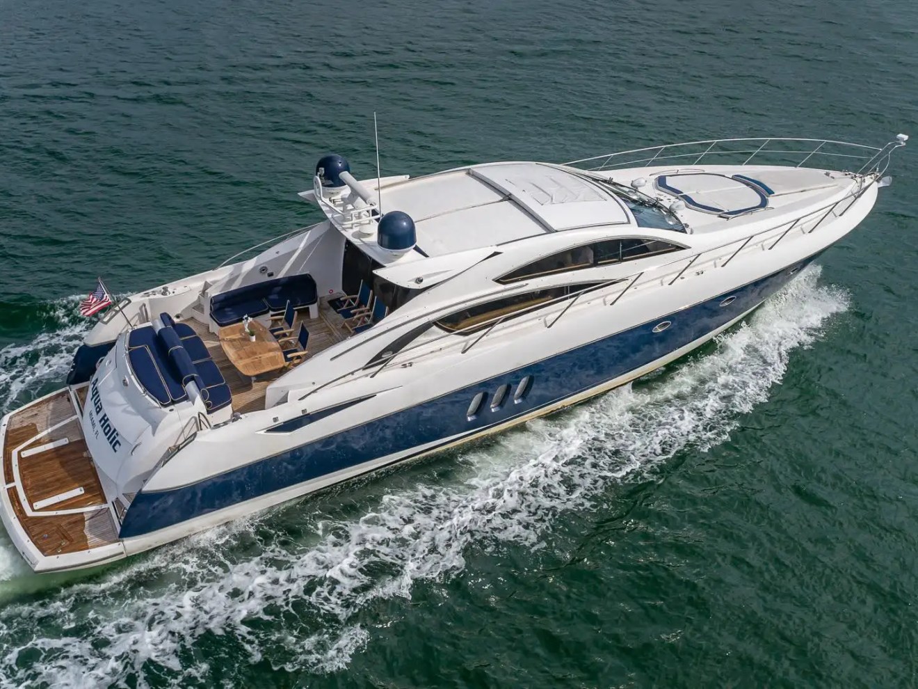 Luxury yacht cruising on open water, viewed from above with waves at the stern.