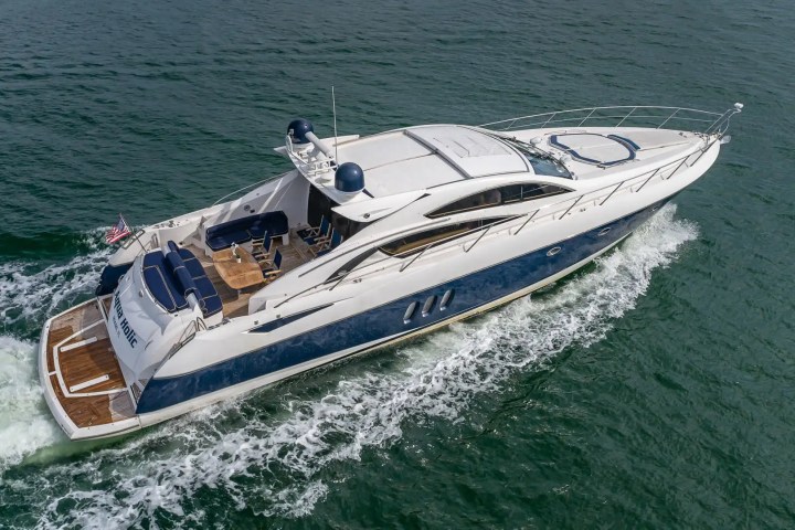 Luxury yacht cruising on open water, viewed from above with waves at the stern.