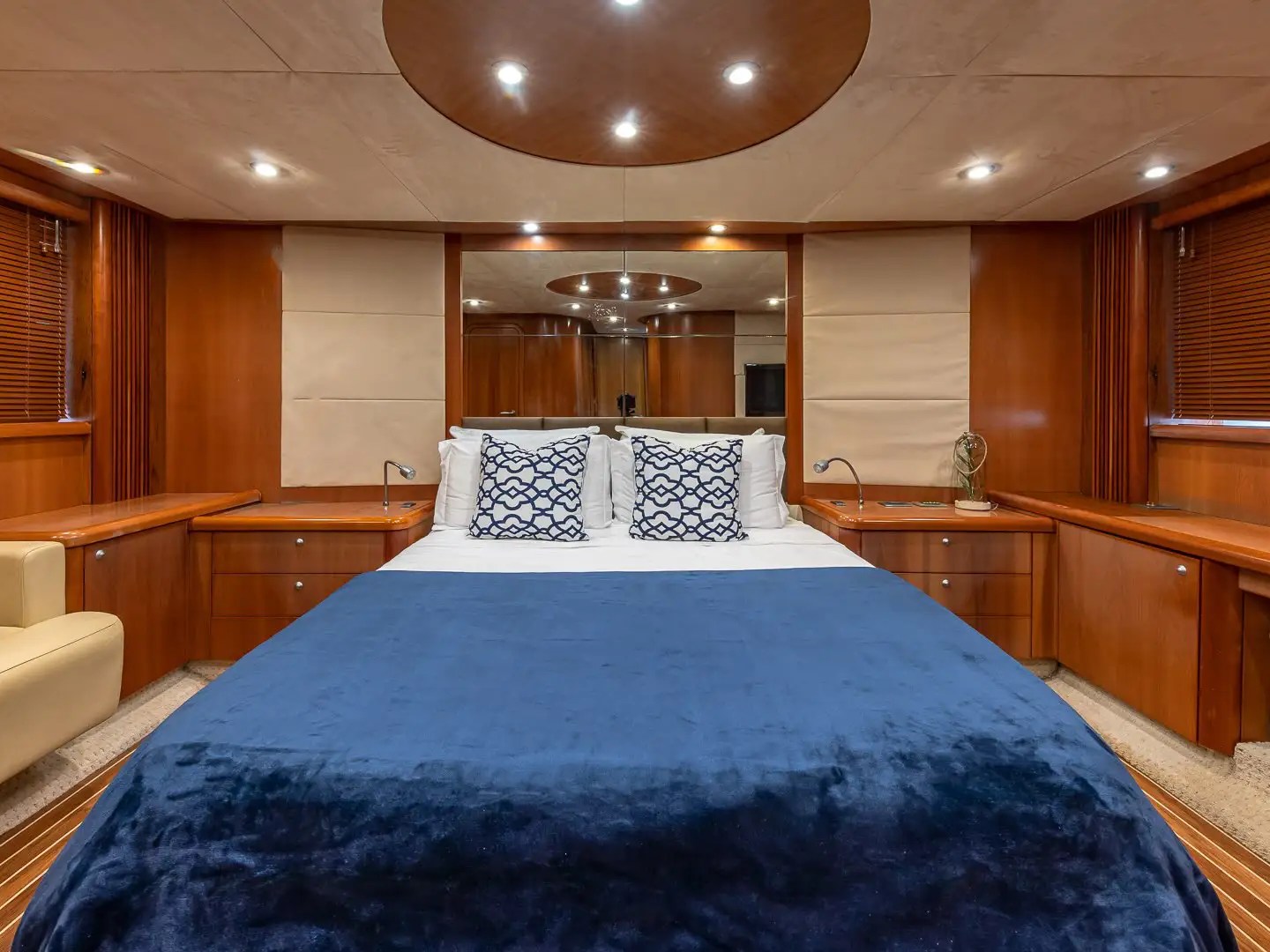 Luxurious ship cabin with bed, blue blanket, wood paneling, and beige armchair.