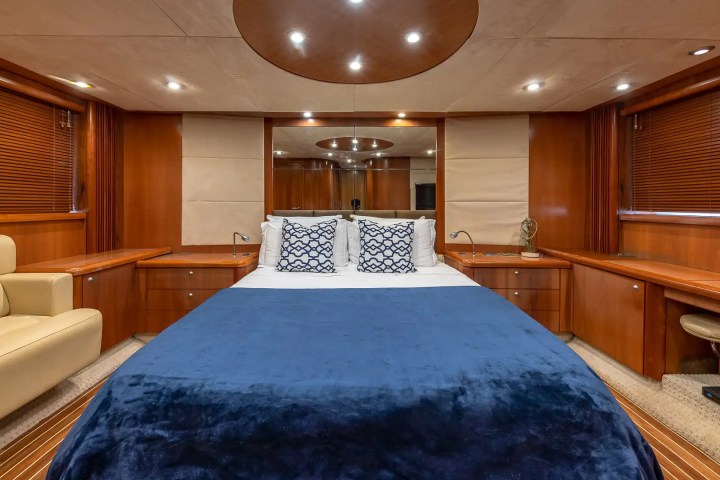 Luxurious ship cabin with bed, blue blanket, wood paneling, and beige armchair.