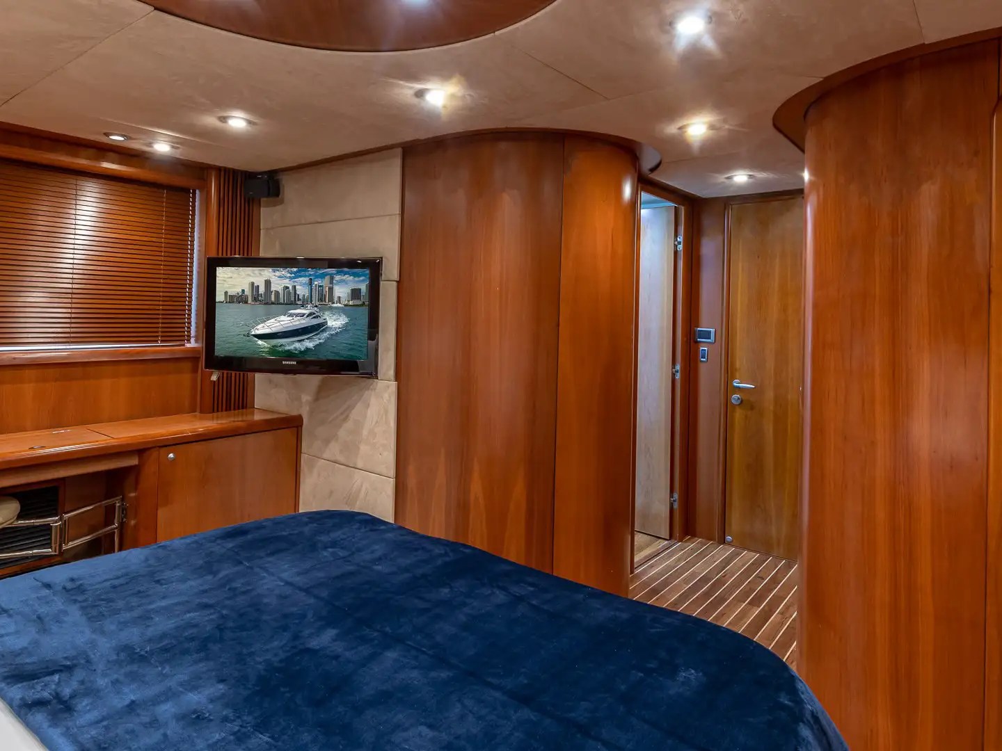 Luxury yacht cabin with wood paneling, TV, blue bedspread, and doors.