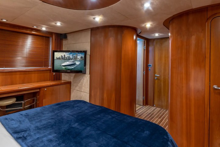 Luxury yacht cabin with wood paneling, TV, blue bedspread, and doors.