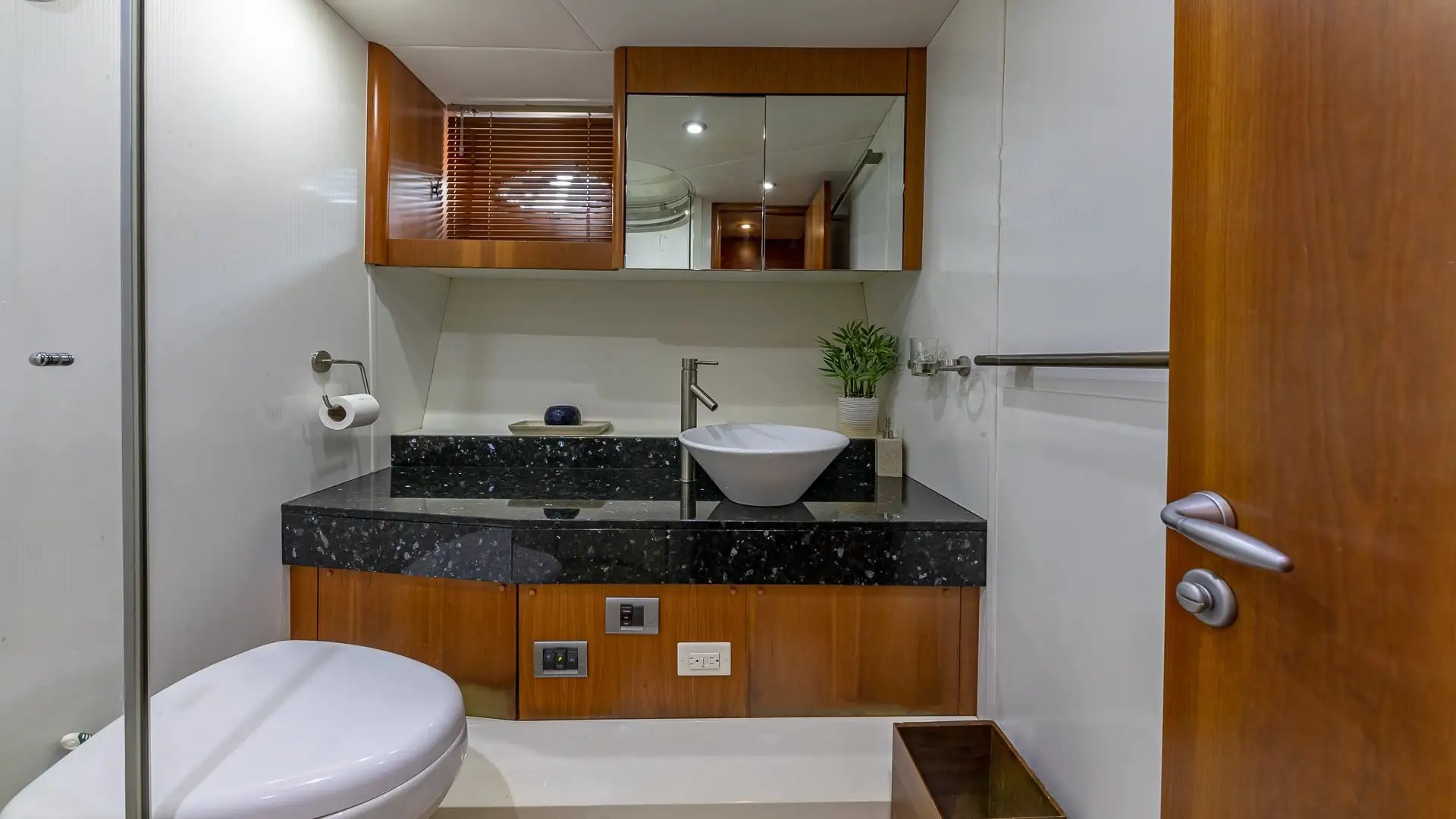 Modern yacht bathroom with sink, toilet, mirror, and wooden accents.