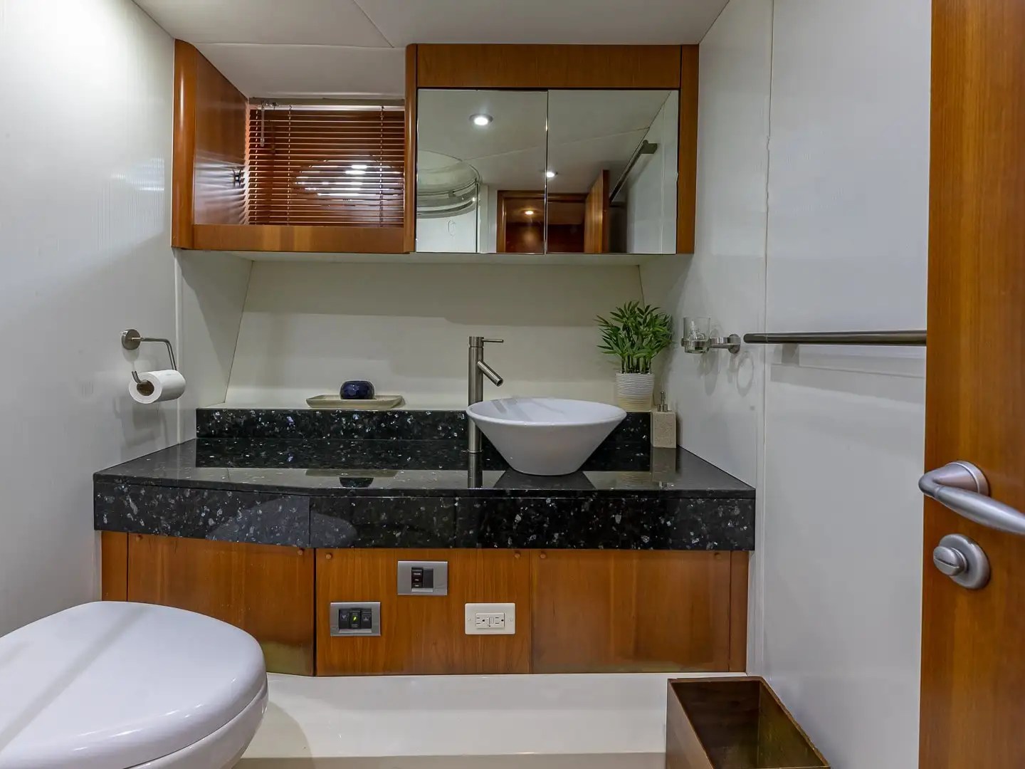Modern yacht bathroom with sink, toilet, mirror, and wooden accents.