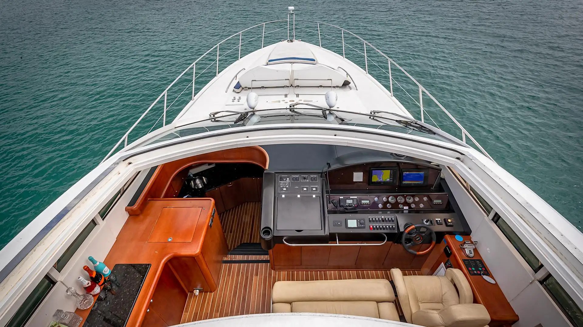 Aerial view of a yacht's cockpit with steering wheel, dashboard, and seating overlooking the water.