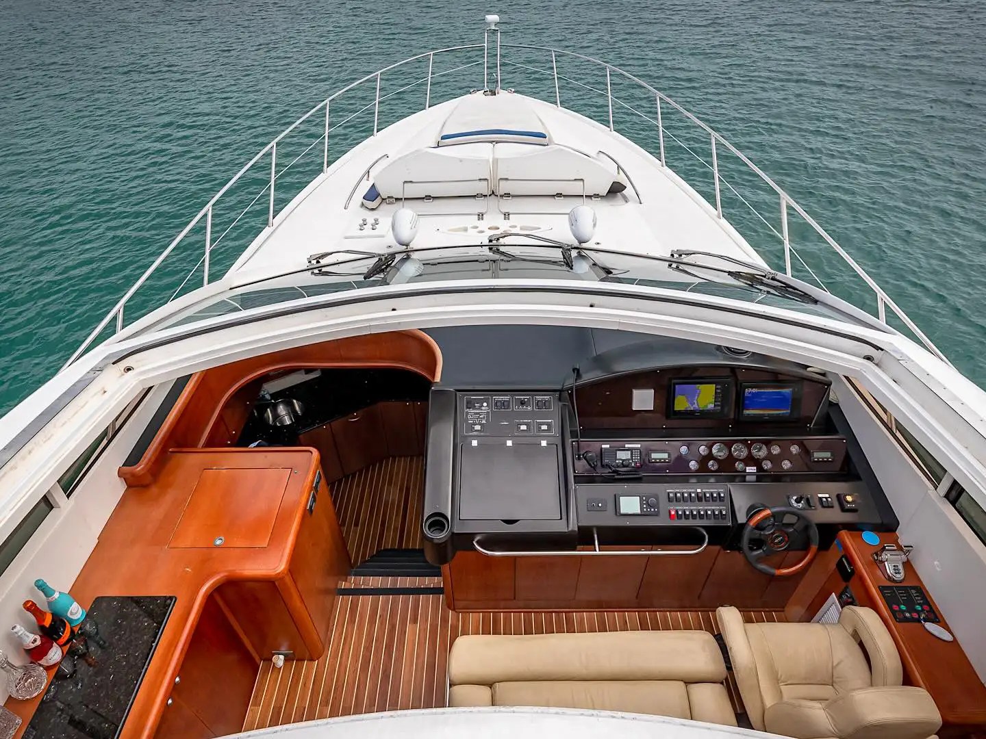 Aerial view of a yacht's cockpit with steering wheel, dashboard, and seating overlooking the water.