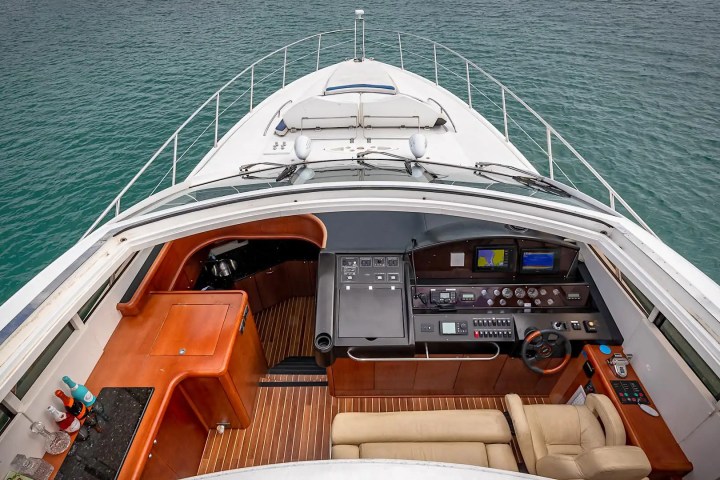 Aerial view of a yacht's cockpit with steering wheel, dashboard, and seating overlooking the water.