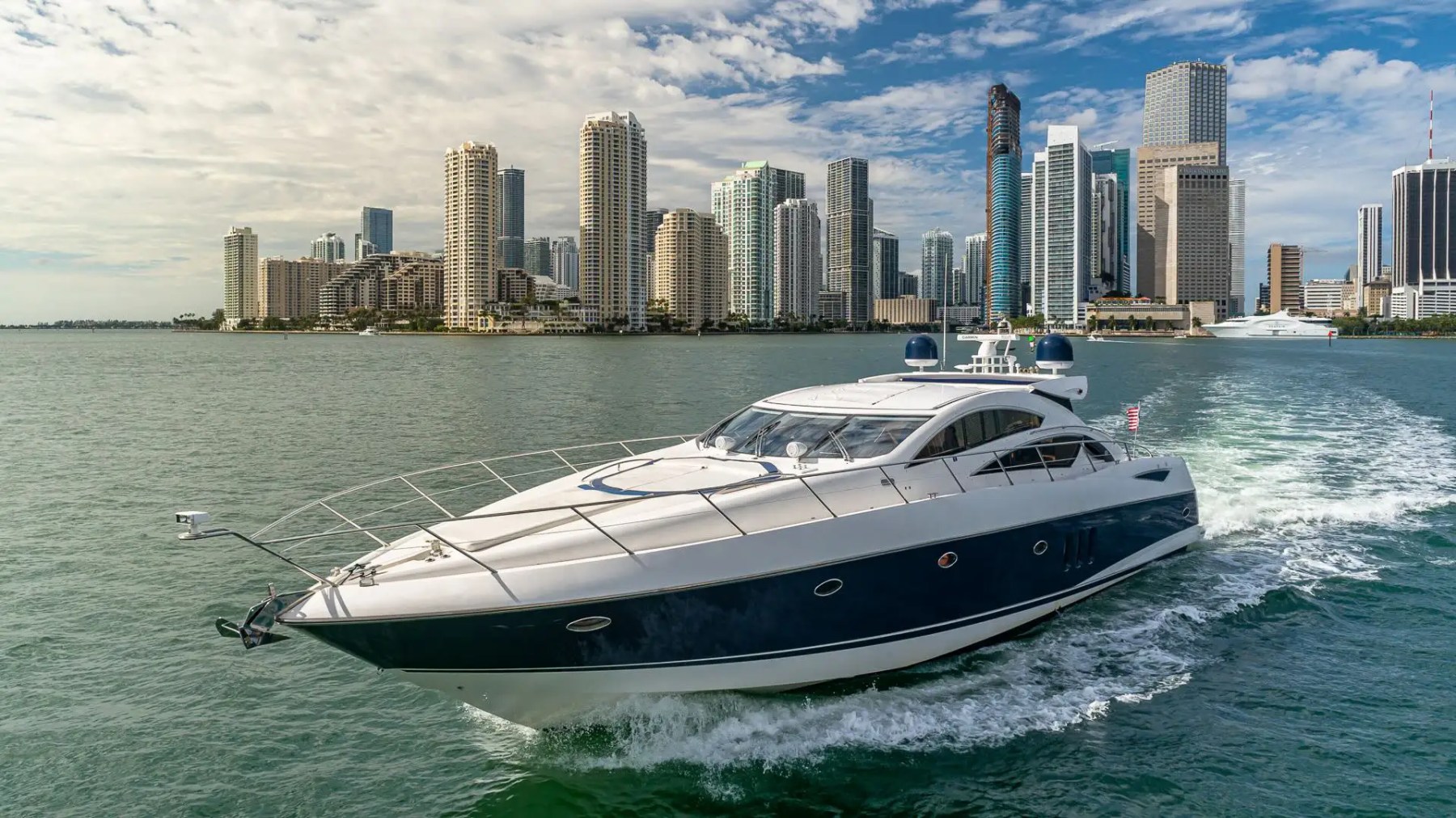 Luxury yacht sailing near a city skyline on a sunny day.