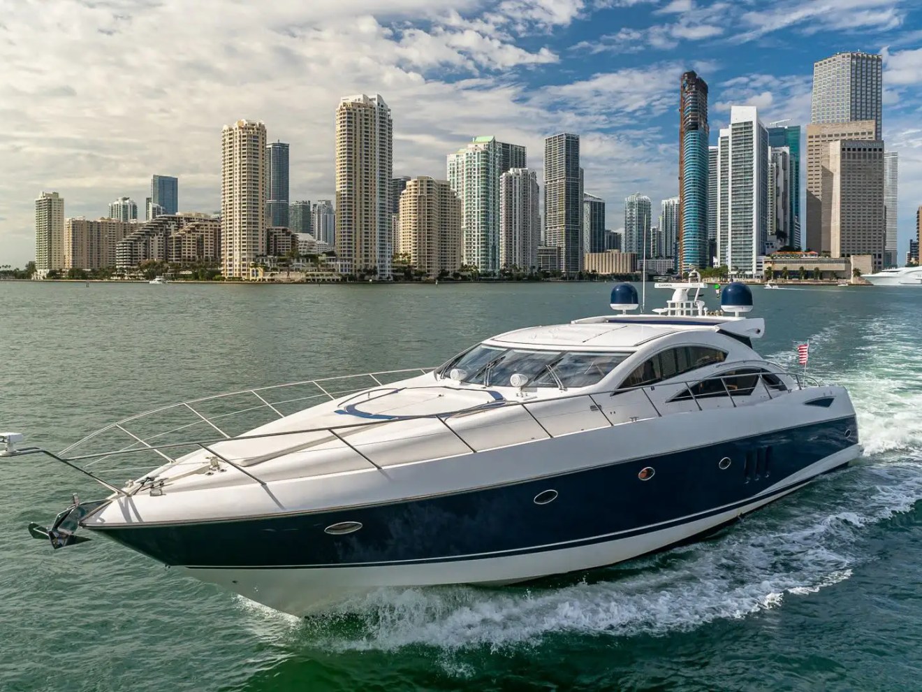 Luxury yacht sailing near a city skyline on a sunny day.
