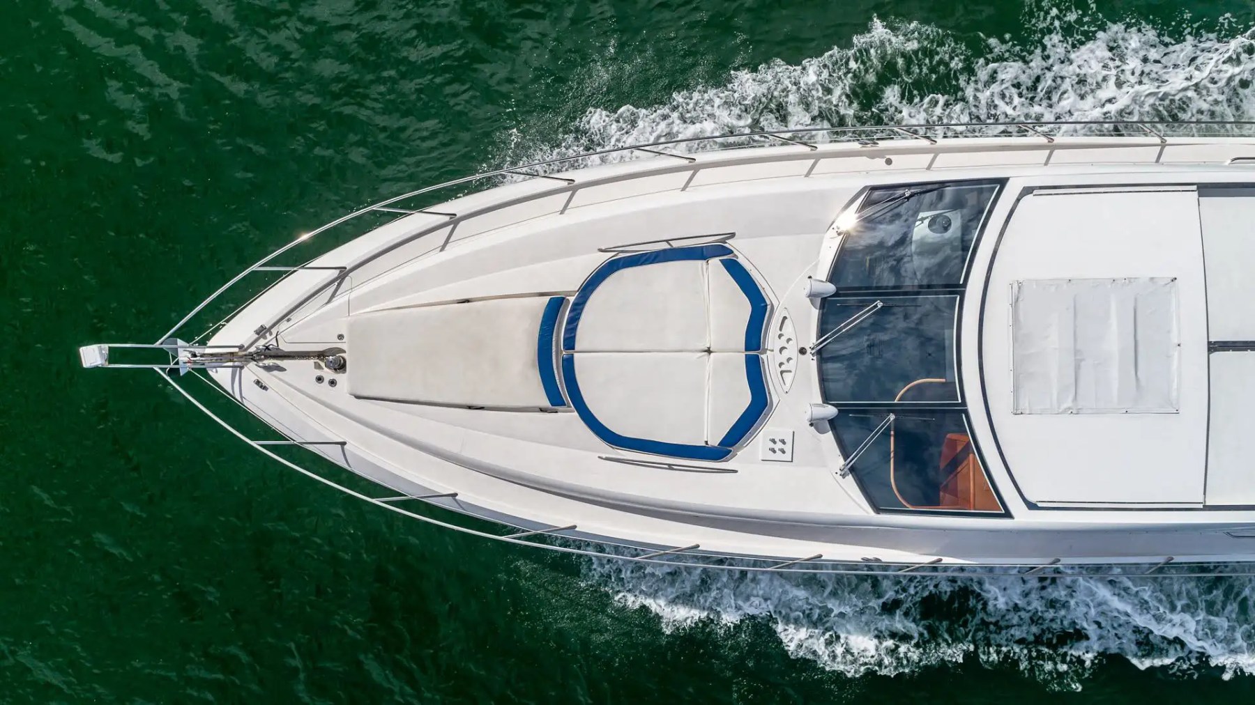 Top view of a speeding white yacht on green water.