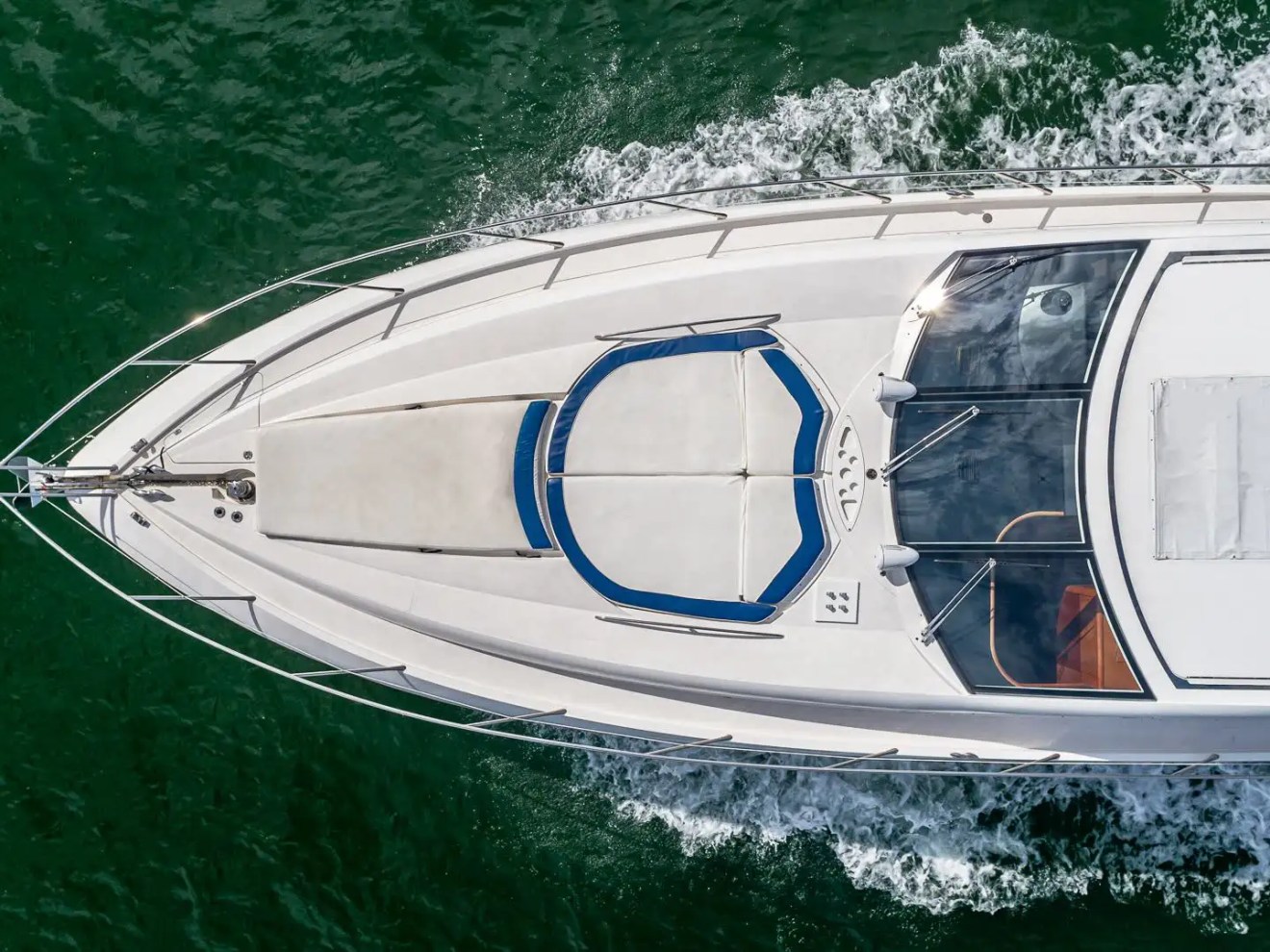 Top view of a speeding white yacht on green water.