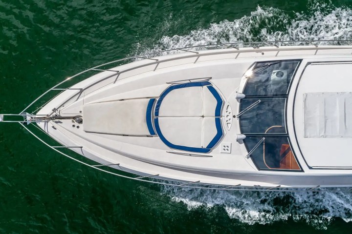 Top view of a speeding white yacht on green water.