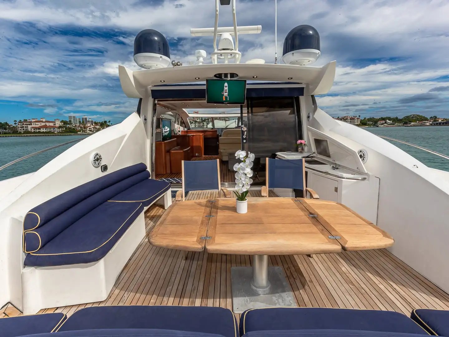 Luxury yacht deck with blue cushioned seating, wooden table, and view of buildings across the water.
