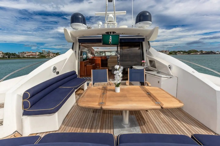 Luxury yacht deck with blue cushioned seating, wooden table, and view of buildings across the water.