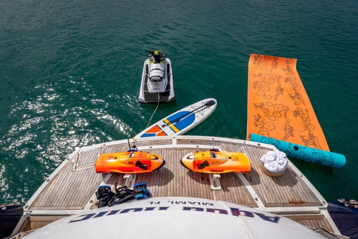 View from yacht deck with jet ski, paddleboard, and orange mat floating on water.