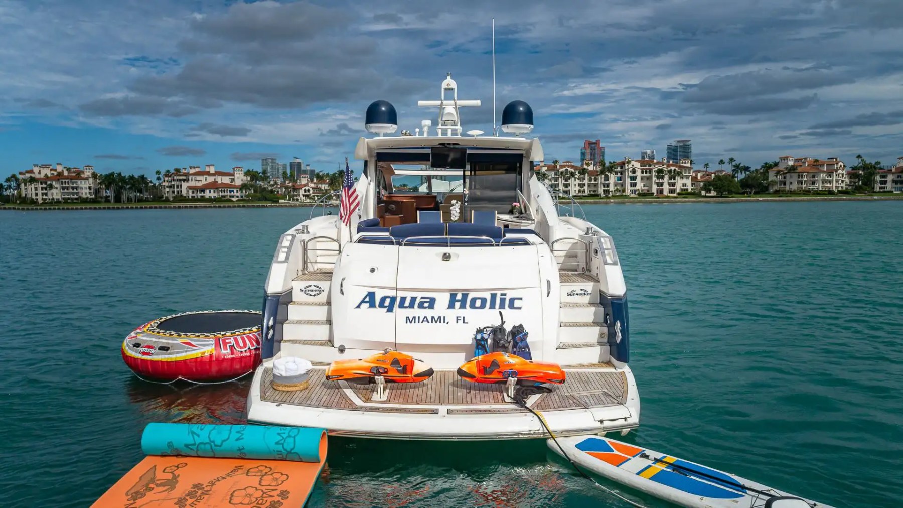 Luxury boat named Aqua Holic with water sports gear docked on calm waters.