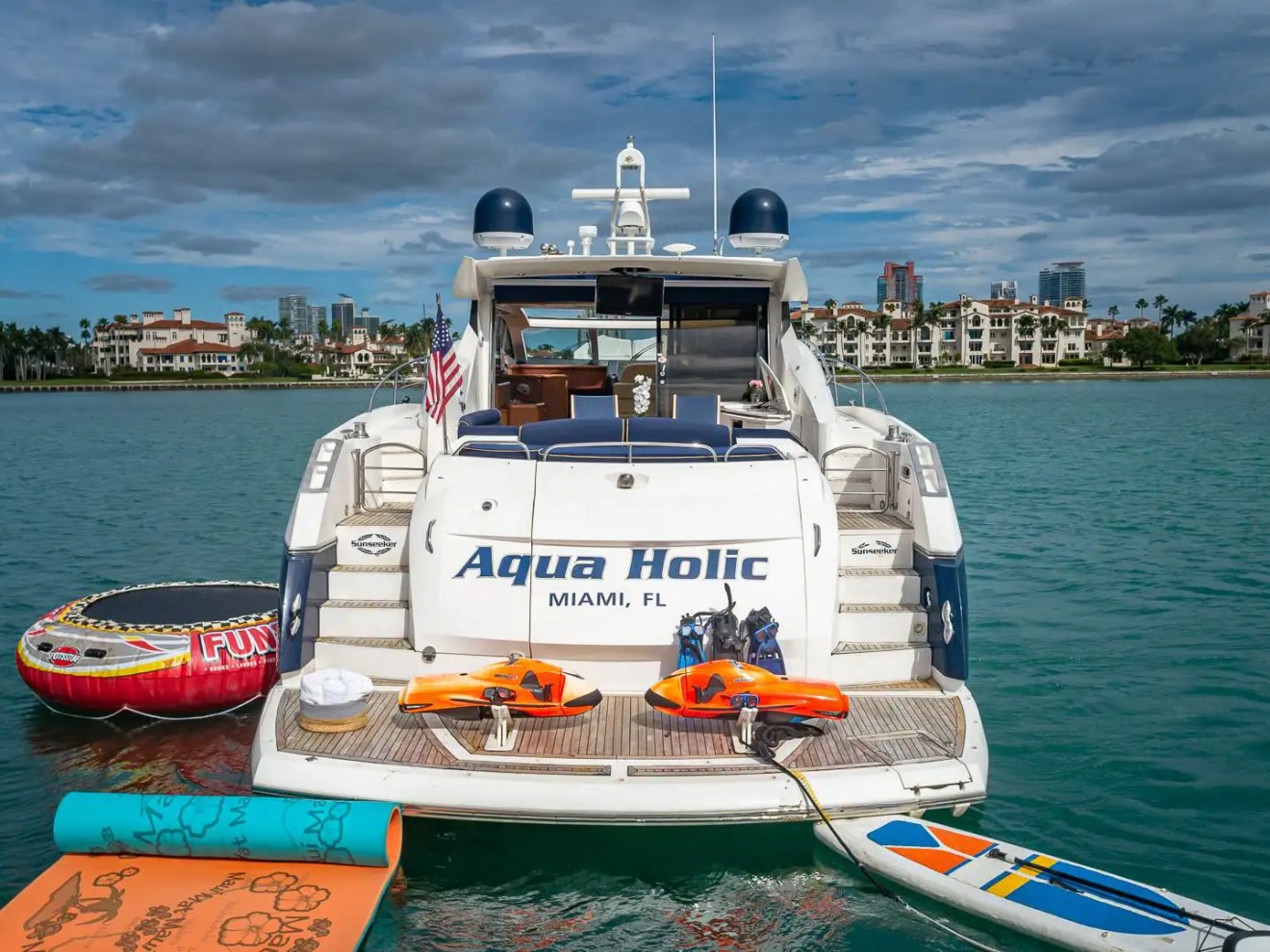 Luxury boat named Aqua Holic with water sports gear docked on calm waters.