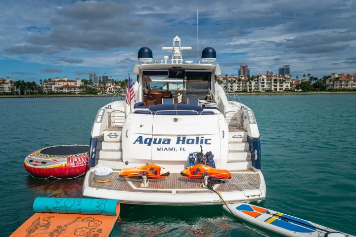 Luxury boat named Aqua Holic with water sports gear docked on calm waters.
