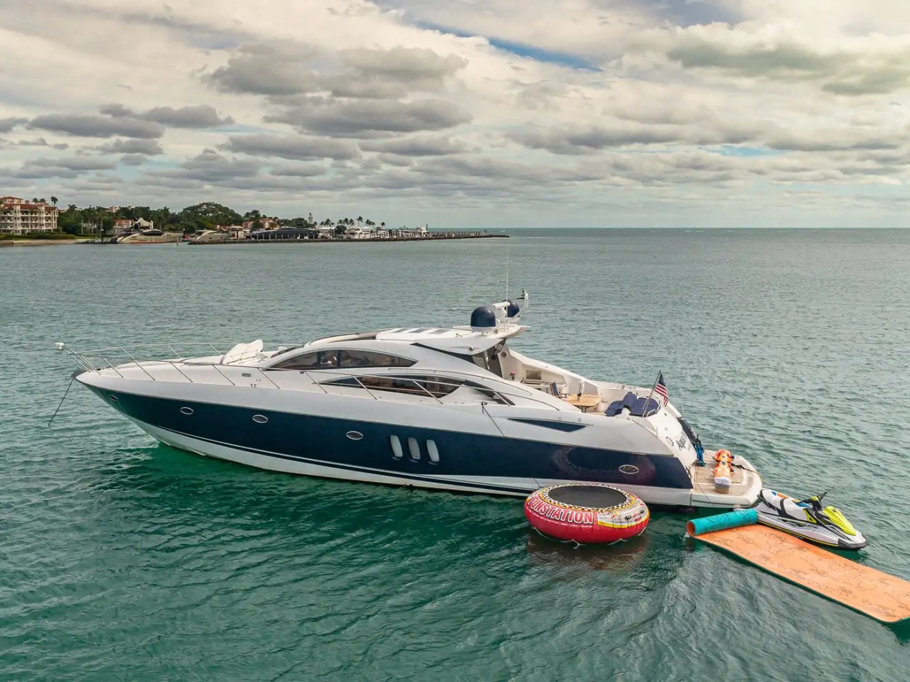 Luxury yacht with inflatable raft and jet ski on calm sea, cloudy sky backdrop.
