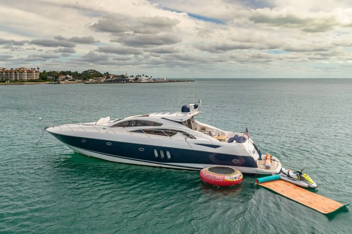 Luxury yacht with inflatable raft and jet ski on calm sea, cloudy sky backdrop.
