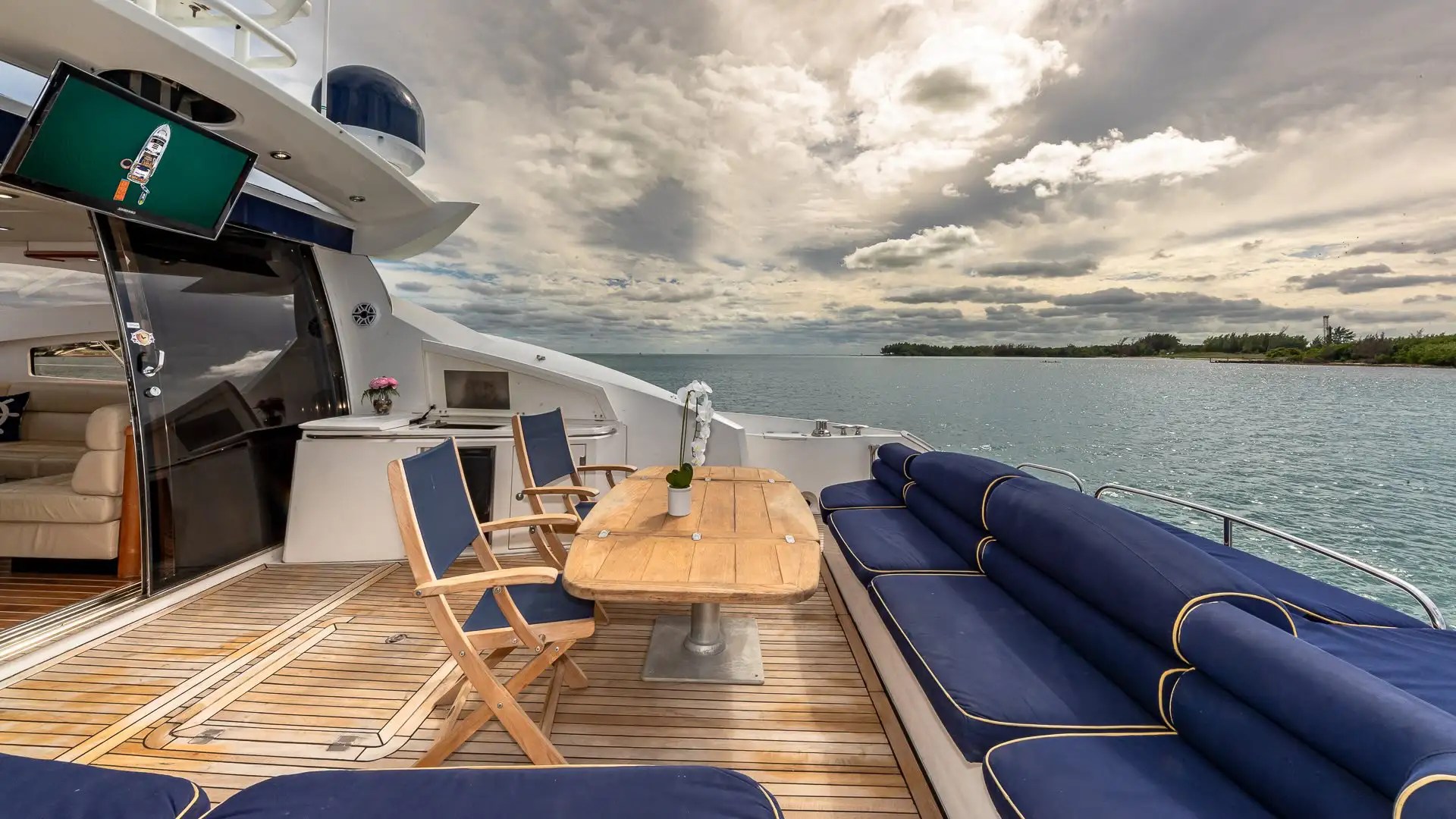 Luxury yacht deck with blue seating, wooden table, and ocean view under a cloudy sky.