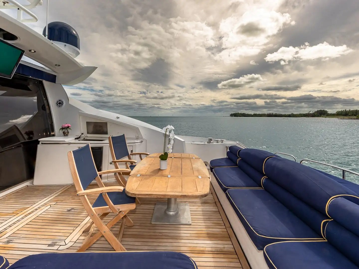 Luxury yacht deck with blue seating, wooden table, and ocean view under a cloudy sky.