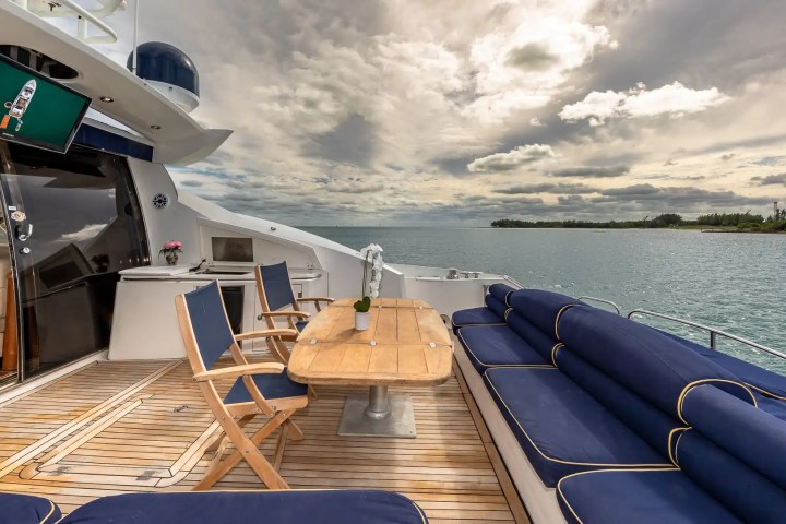 Luxury yacht deck with blue seating, wooden table, and ocean view under a cloudy sky.