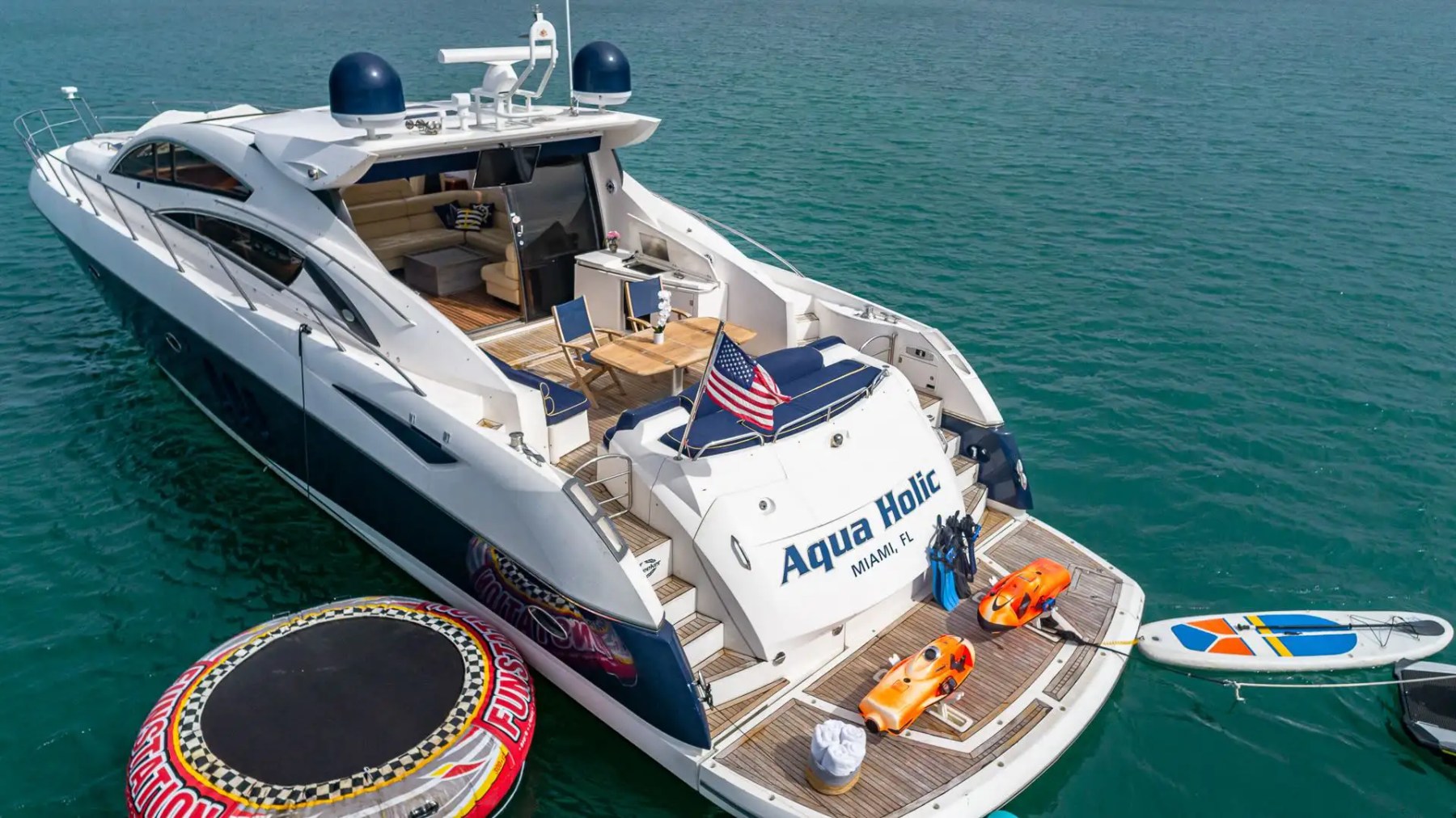 Luxury yacht 'Aqua Holic' with water toys and American flag in blue ocean.