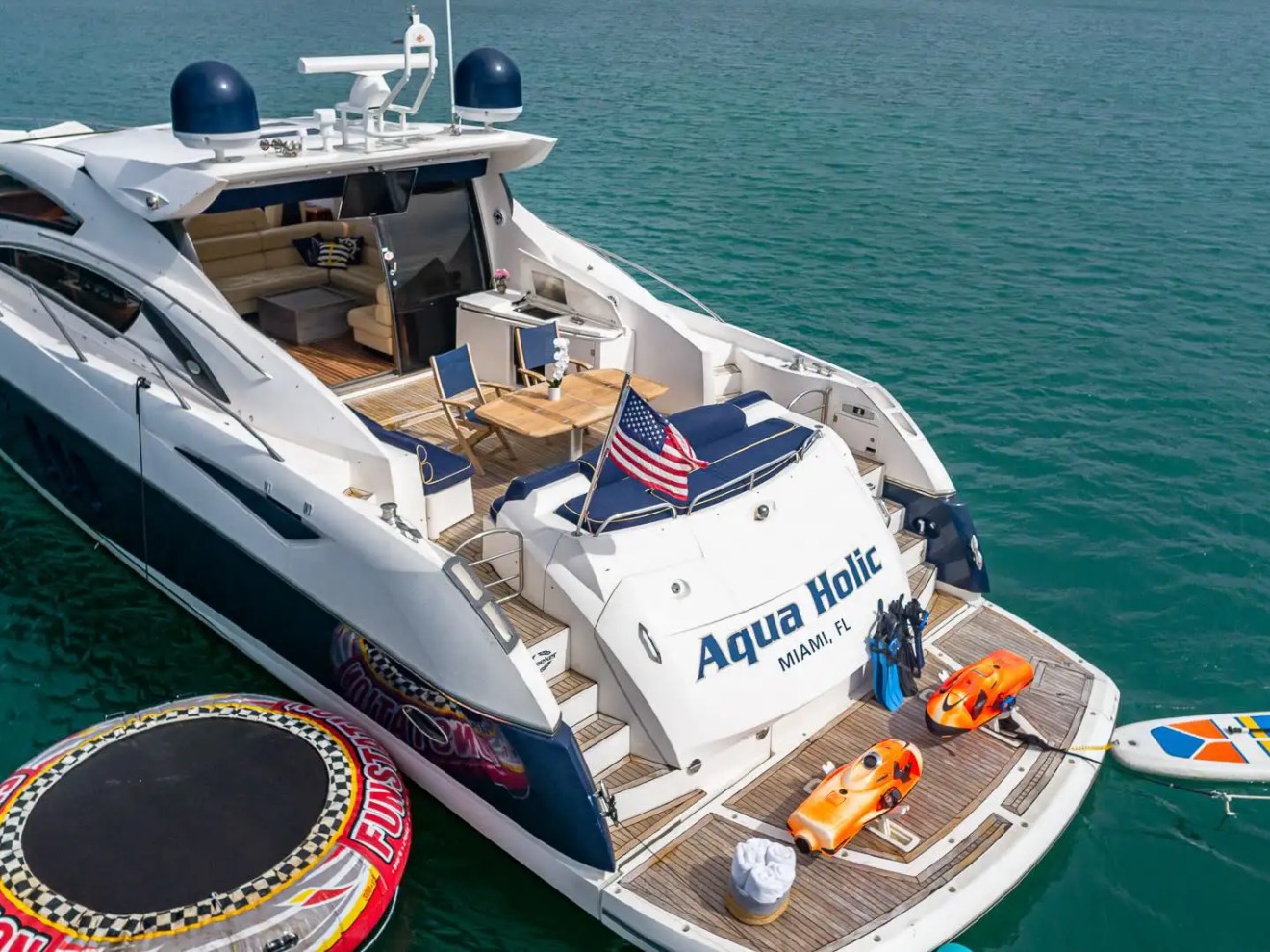 Luxury yacht 'Aqua Holic' with water toys and American flag in blue ocean.