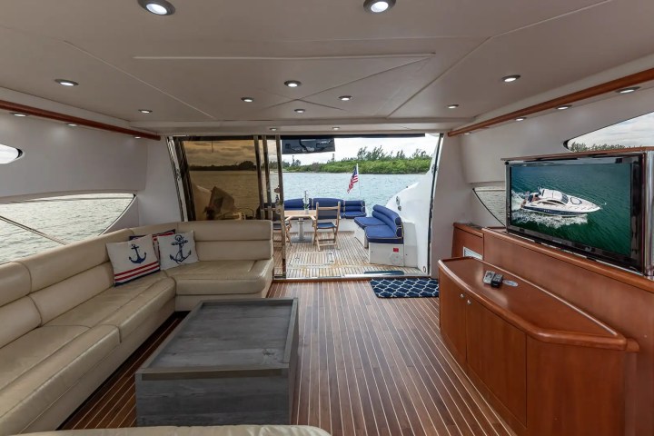 Luxurious yacht interior with beige sofas, TV, and wooden floor, overlooking water.