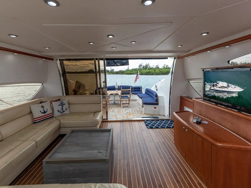 Luxurious yacht interior with beige sofas, TV, and wooden floor, overlooking water.