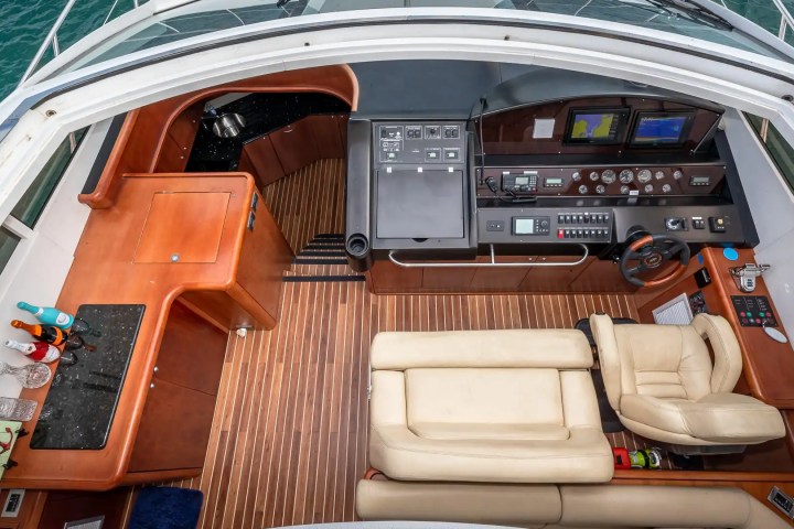 Boat cockpit with steering wheel, control panels, and beige seating on polished wood floor.