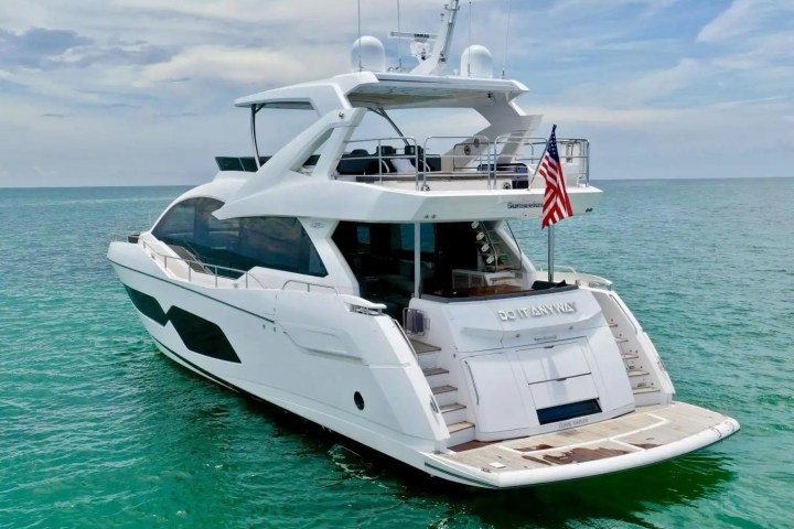 Luxury yacht with American flag anchored in turquoise sea under a cloudy sky.
