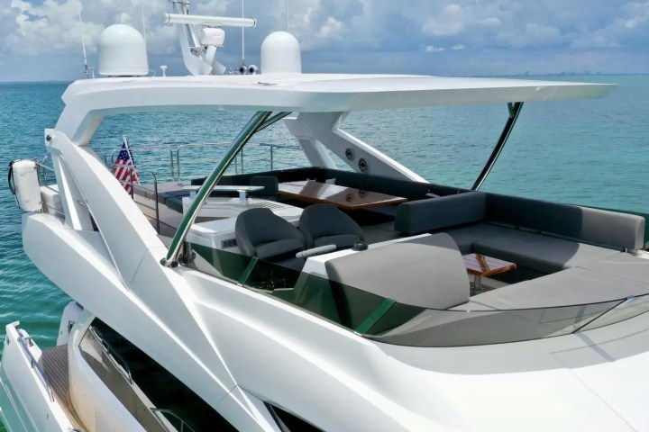 Luxury yacht deck with seating area, tables, and American flag on a sunny day at sea.