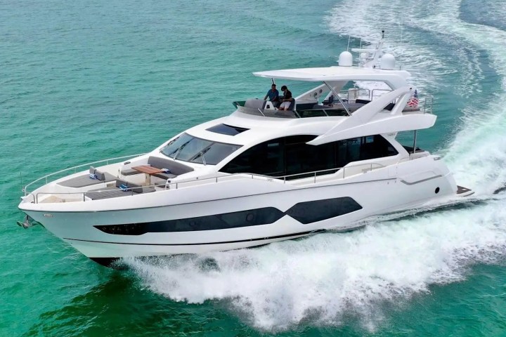 White yacht cruising on turquoise water with people on deck.