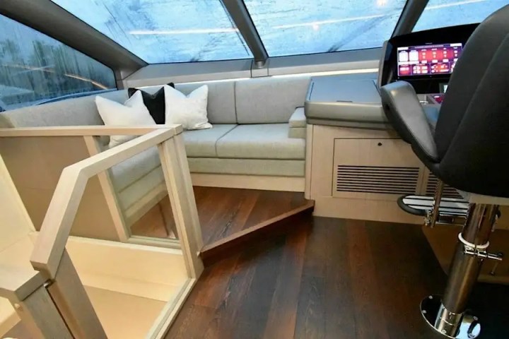 Modern yacht interior with sofa, control panel, and captain's chair.