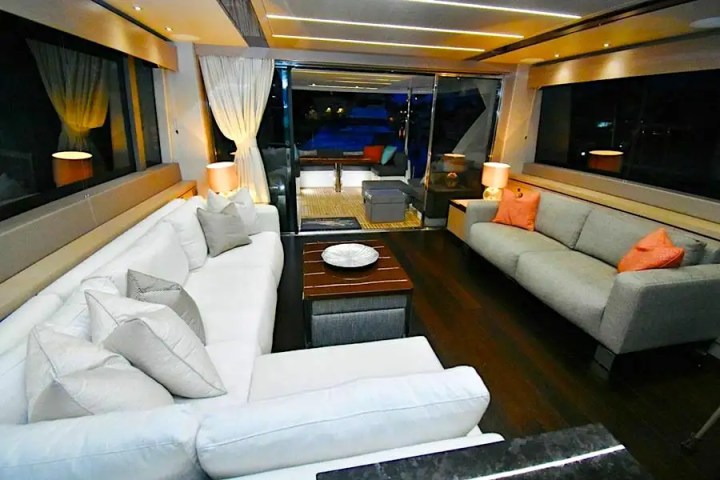 Luxury yacht interior with white and gray sofas, accented with pillows and ambient lighting.