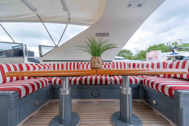 Boat deck with striped red cushions, wooden table, and potted plant under canopy.