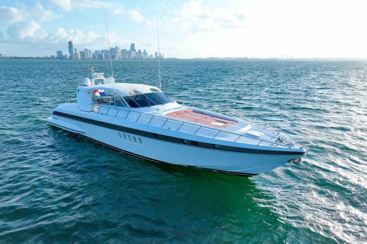 A large white yacht on the water with a city skyline in the background under a blue sky.