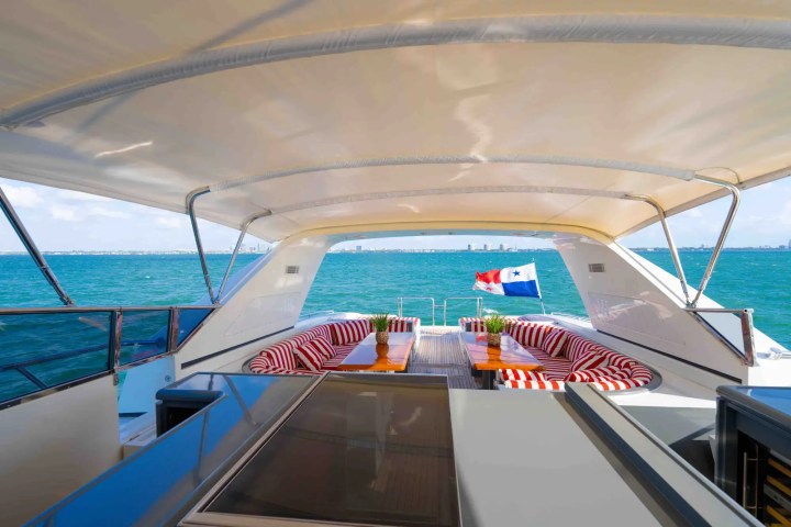 View from yacht deck with striped seating, tables, and a flag over blue water.