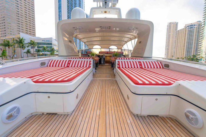 Luxury yacht deck with red and white striped cushions in city marina.