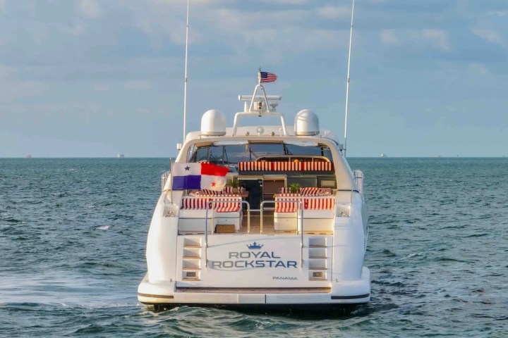 Luxury yacht 'Royal Rockstar' with flags, sailing on the ocean under a partly cloudy sky.