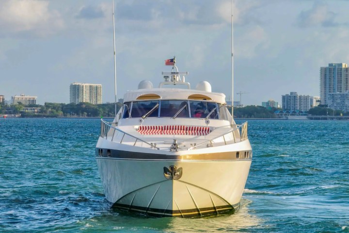 Front view of a yacht on water with city skyline in the background.