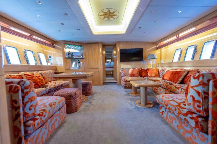 Luxurious yacht interior with orange patterned sofas, wooden accents, and multiple windows.