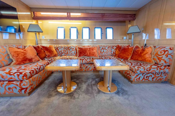 Luxurious yacht interior with ornate orange sofas, two tables, and modern lamps.