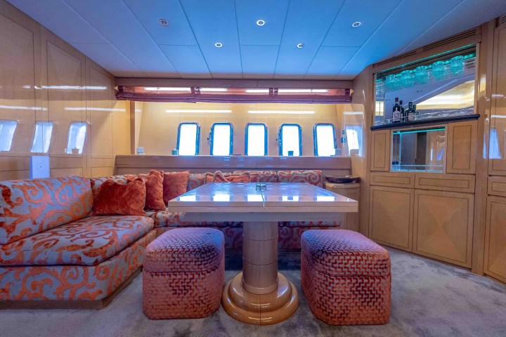 Luxury yacht lounge with orange patterned seating, plush cushions, and a wooden table near windows.