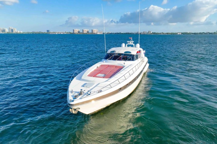Luxury yacht on calm sea with city skyline in background under blue sky with clouds.